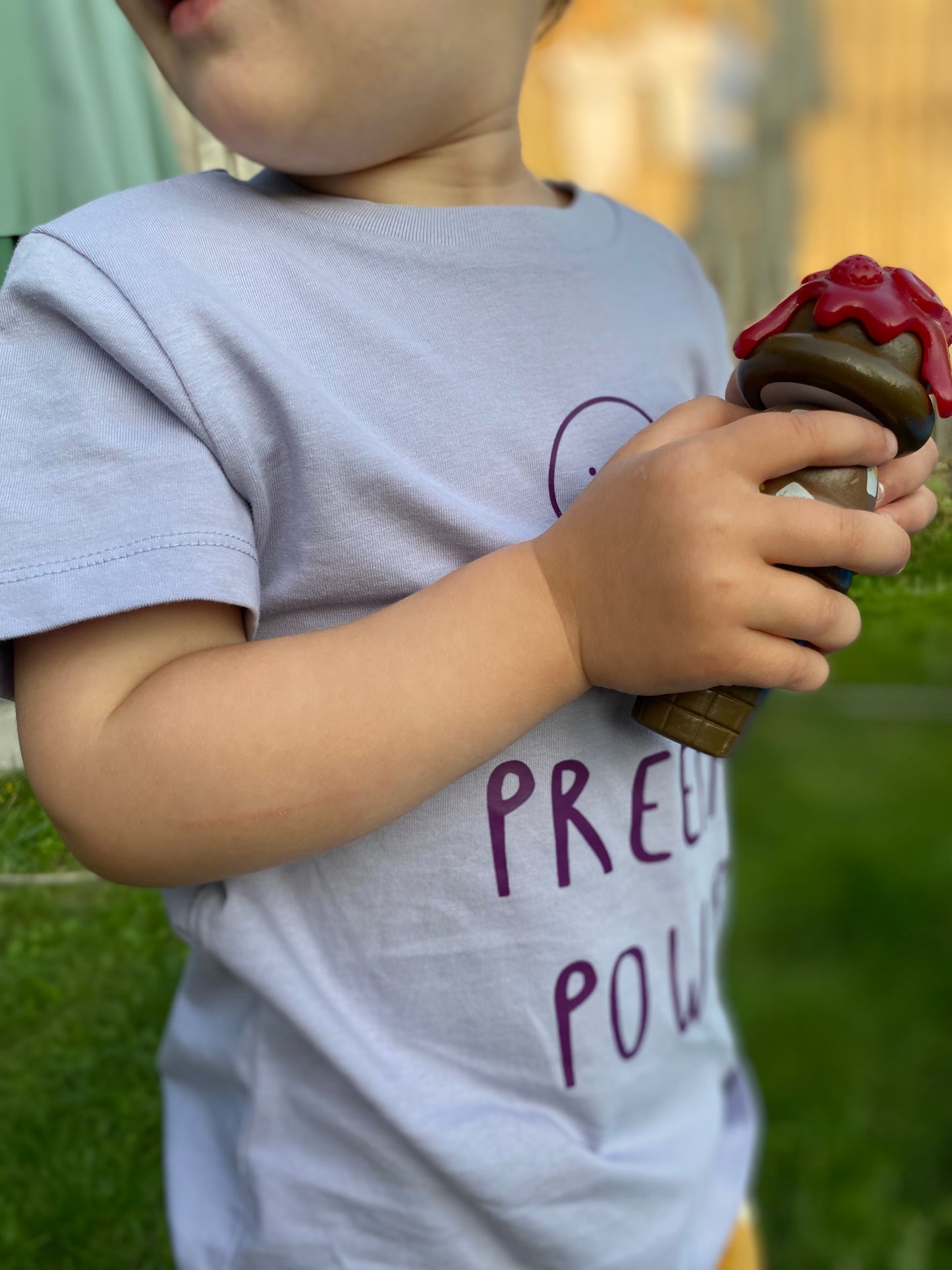 Child holding a toy ice cream cone outdoors with preemie power tshirt on