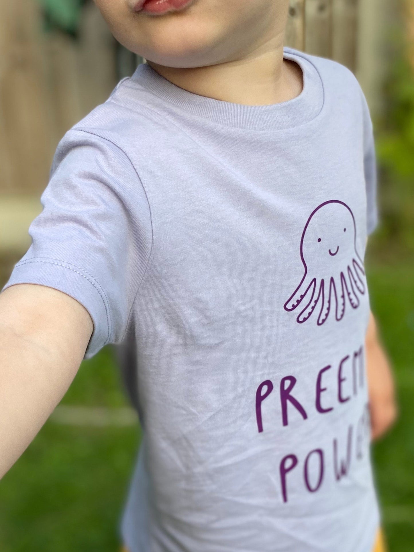 Child wearing a purple t-shirt with text and yellow shorts outdoors