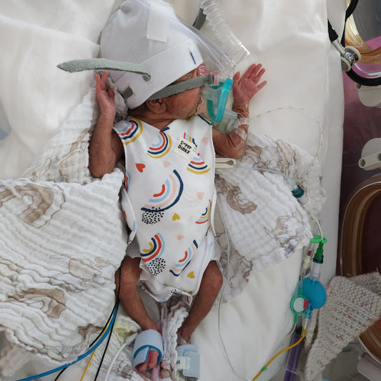 Premature baby on CPAP wearing a hat and SuperDinky Rainbow NICU baby vest